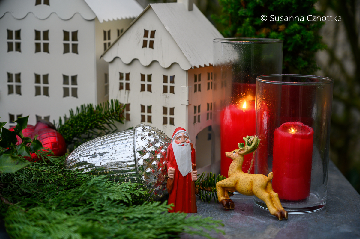 Kleiner Weihnachtsmann und kleines Rentier aus Holz neben roten Kerzen