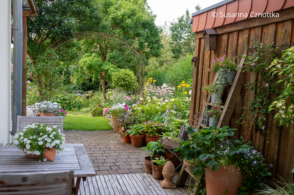 Gartenraum: eine kleine intime Terrasse mit einer kleinen Sitzgruppe und vielen Blumentöpfen