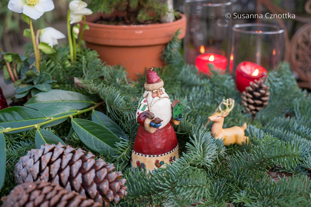 Kleine Weihnachtsmann- und Rentierfiguren zwischen weihnachtlichem Grün
