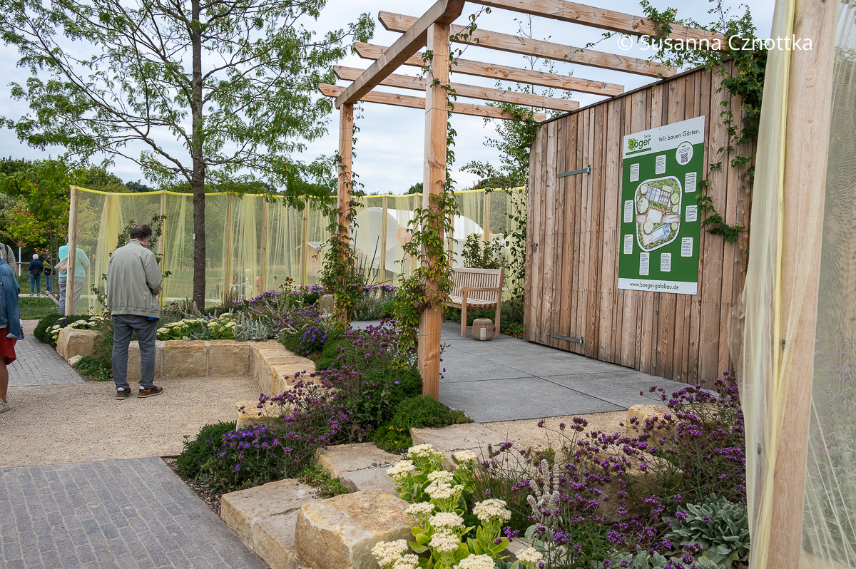 Eine schlichte Pergola in einem Schaugarten auf der Landesgartenschau Niedersachsen 2026 Ein Schaugarten mit einer schlichten Holzpergola und Einfassungen aus hellem Naturstein