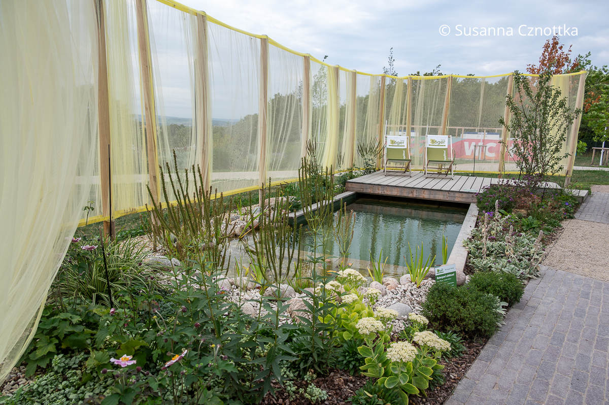 Ein kleiner Naturpool mit Holzdeck in einem Schaugarten Ein kleiner Naturpool mit Holzdeck in einem Schaugarten