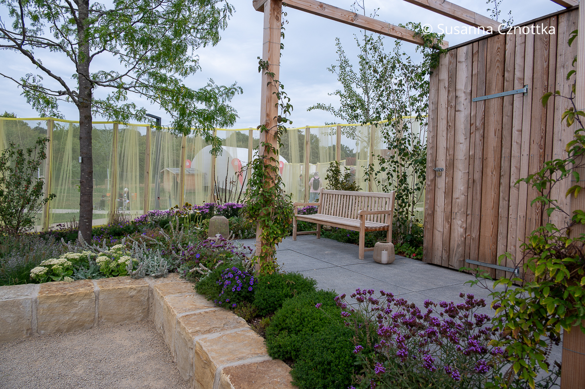 Ein Gartenraum mit Pergola und hellem Naturstein Ein Gartenraum mit hellem Naturstein und einer Pergola aus hellem Holz
