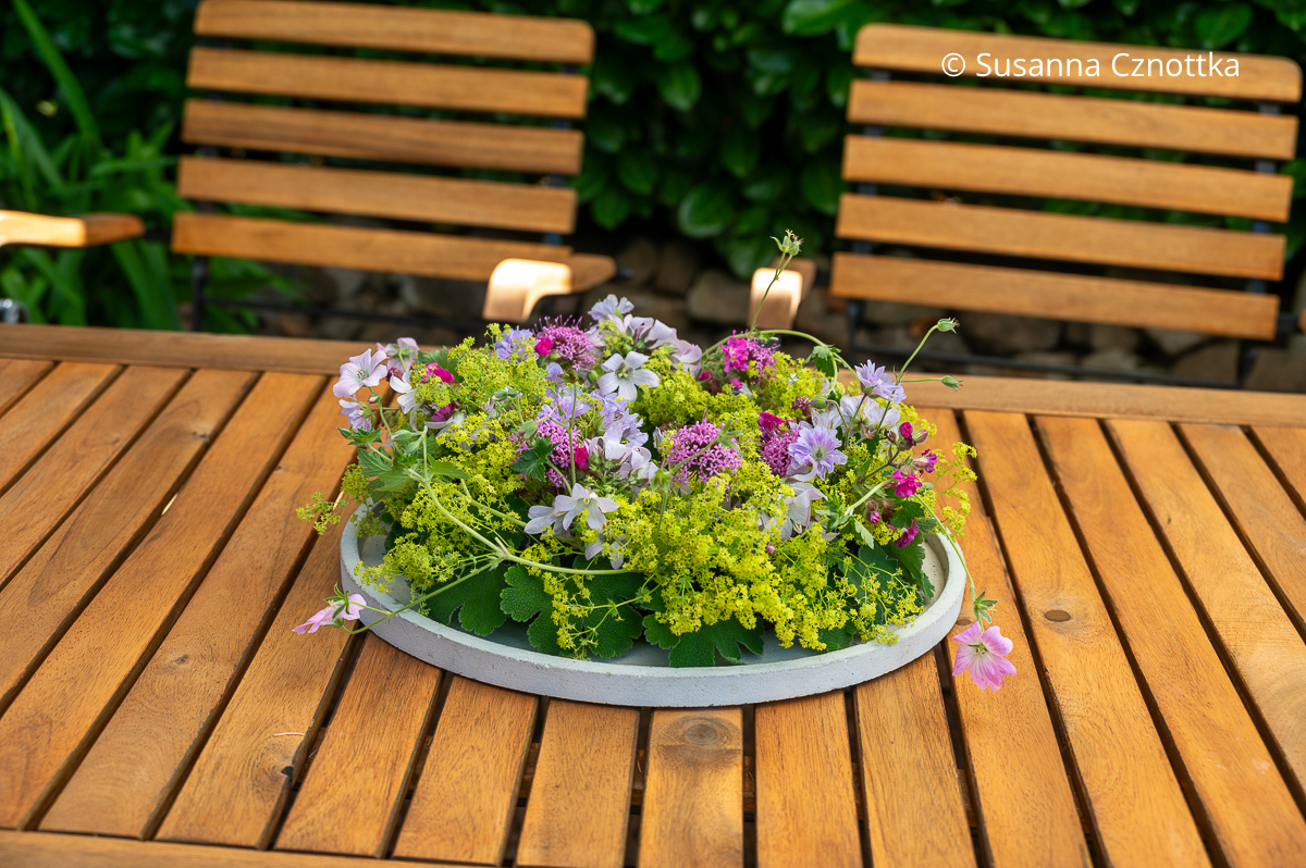 Ein Gesteck aus Frauenmantel, Spornblumen und Storchschnabel auf einem Gartentisch Ein Gesteck aus Frauenmantel, Spornblumen und Storchschnabel auf einem Gartentisch