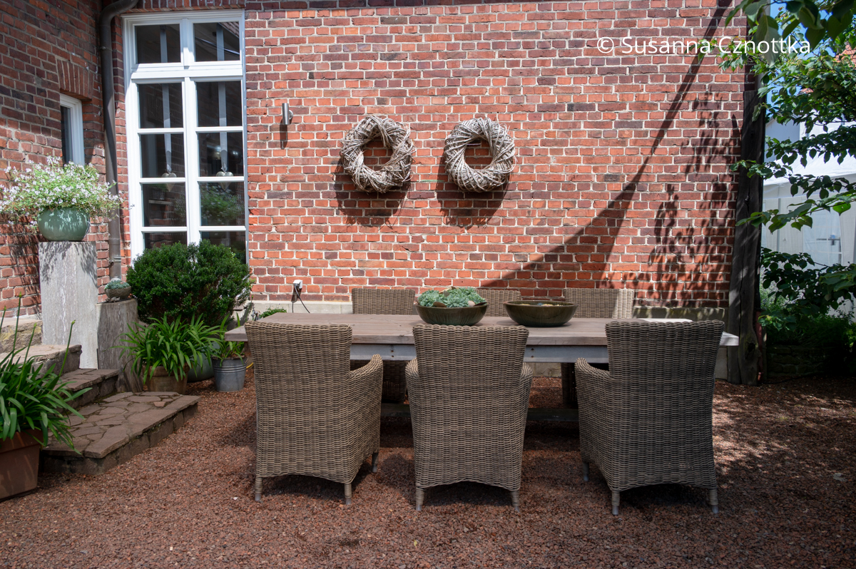 Ein Gartentisch mit Korbstühlen vor einer Backsteinwand Ein Gartentisch mit Korbstühlen vor einer Backsteinwand