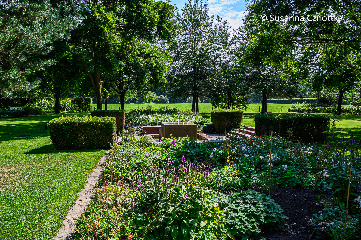 Ein quadratischer Senkgarten mit einem würfelförmigen Wasserspiel und Buchsbaumquadern an allen vier Ecken