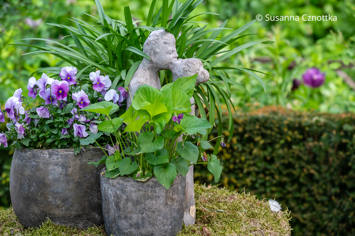 Eine kleine Skulptur eines sich küssenden Paares zwischen Pflanzen in Töpfen
