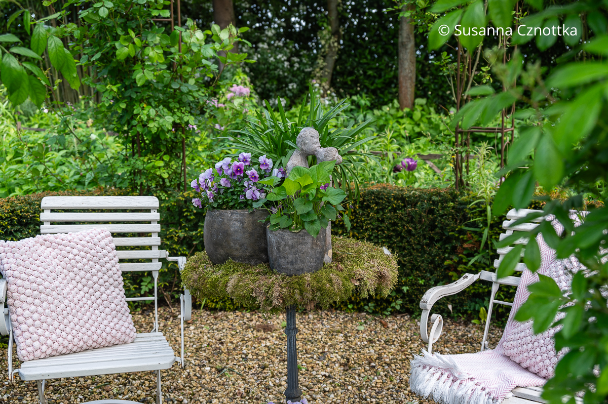 Gartendekoration: ein romantisches Arrangement aus Veilchen in Töpfen und einer steinernen Figur
