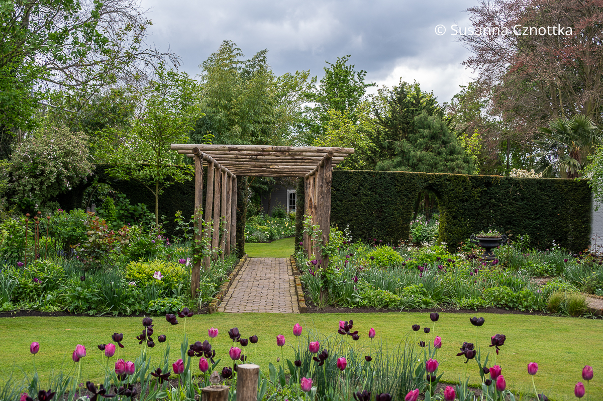 Gartengestaltung: Eine Pergola und ein gepflasterter Weg bilden eine Sichtachse zwischen zwei Gartenräumen.