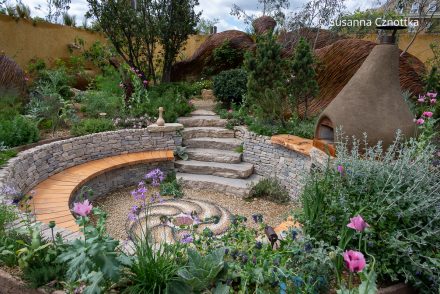 Senkgarten im Freedom From Torture (Freiheit von Folter) Garten auf der Chelsea Flower Show 2024 mit Natursteinmauer, einer langgezogenen Holzbank und einem Lehmofen