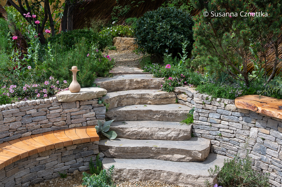 Eine Treppe aus hellen, unregelmäßigen Steinplatten führt in einen Senkgarten