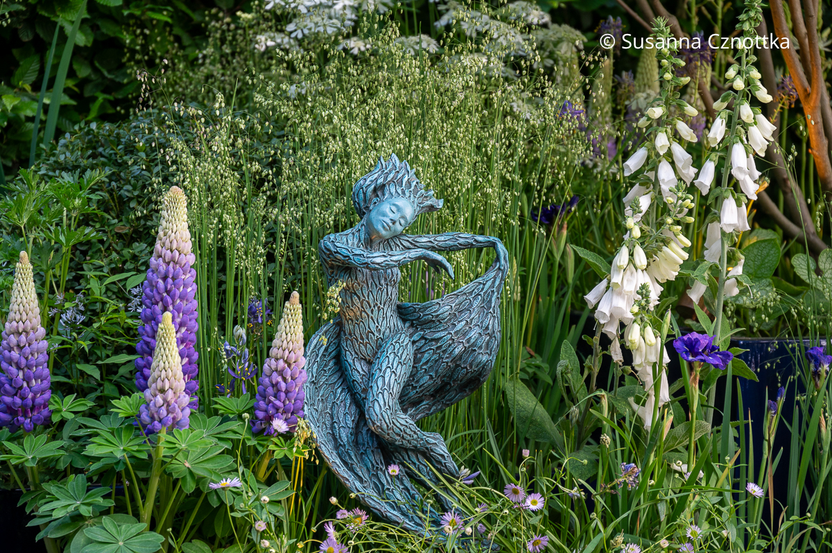 Verspielter Garten: Figur einer Nymphe zwischen Lupinen uns Fingerhut