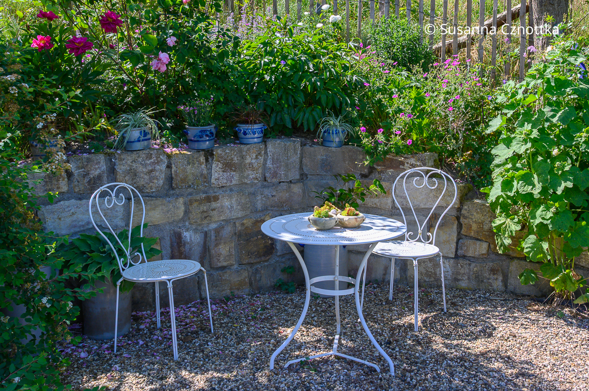 Leichte Gartenmöbel aus Metall passen zum mediterranen Gartenstil Leichte weiße Gartenmöbel aus Metall vor einer Natursteinmauer