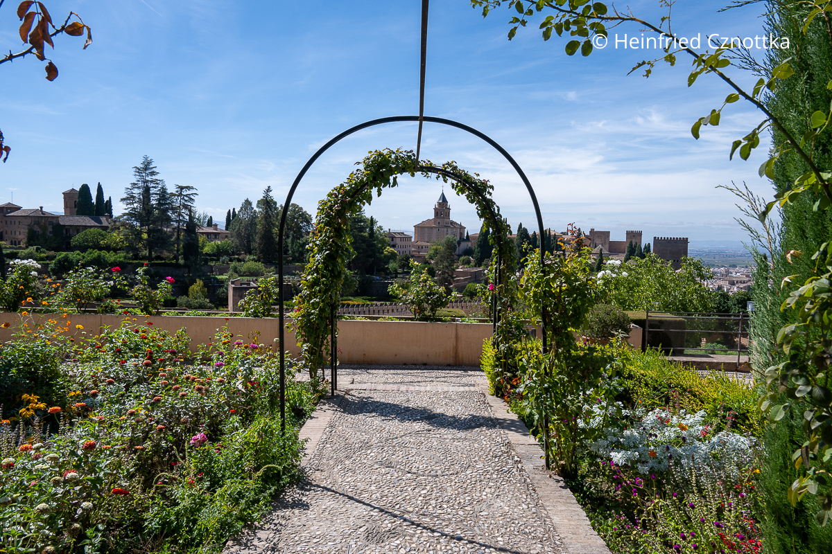 Ein Gartenbereich im Palacio de Generalife, Granada, mit abgesenkten Beeten und Blick auf die Alhambra und die Kirche Santa Maria de la Alhambra