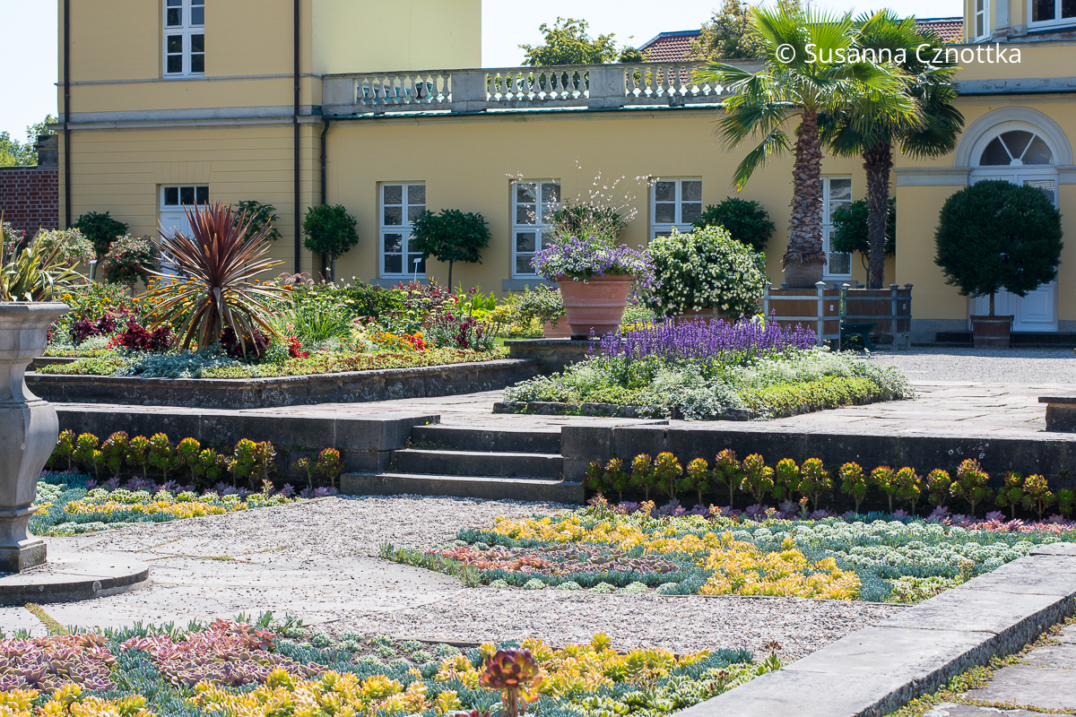 Ausschnitt aus dem Senkgarten mit der Sonnenuhr im Berggarten Hannover vor dem gelb gestrichenen Bibliothekspavillon