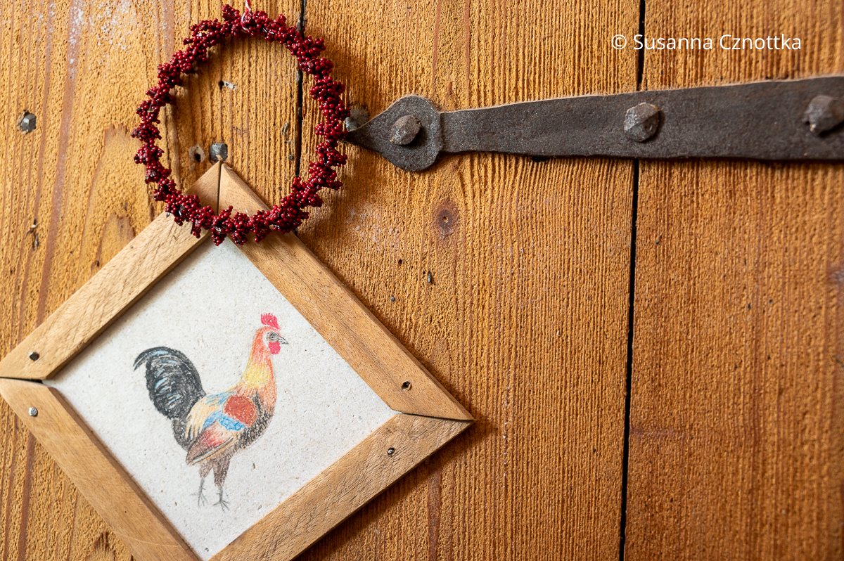Dekoration an einer alten Tür: eine Zeichnung eines Hahns und ein Kränzchen aus roten Beeren