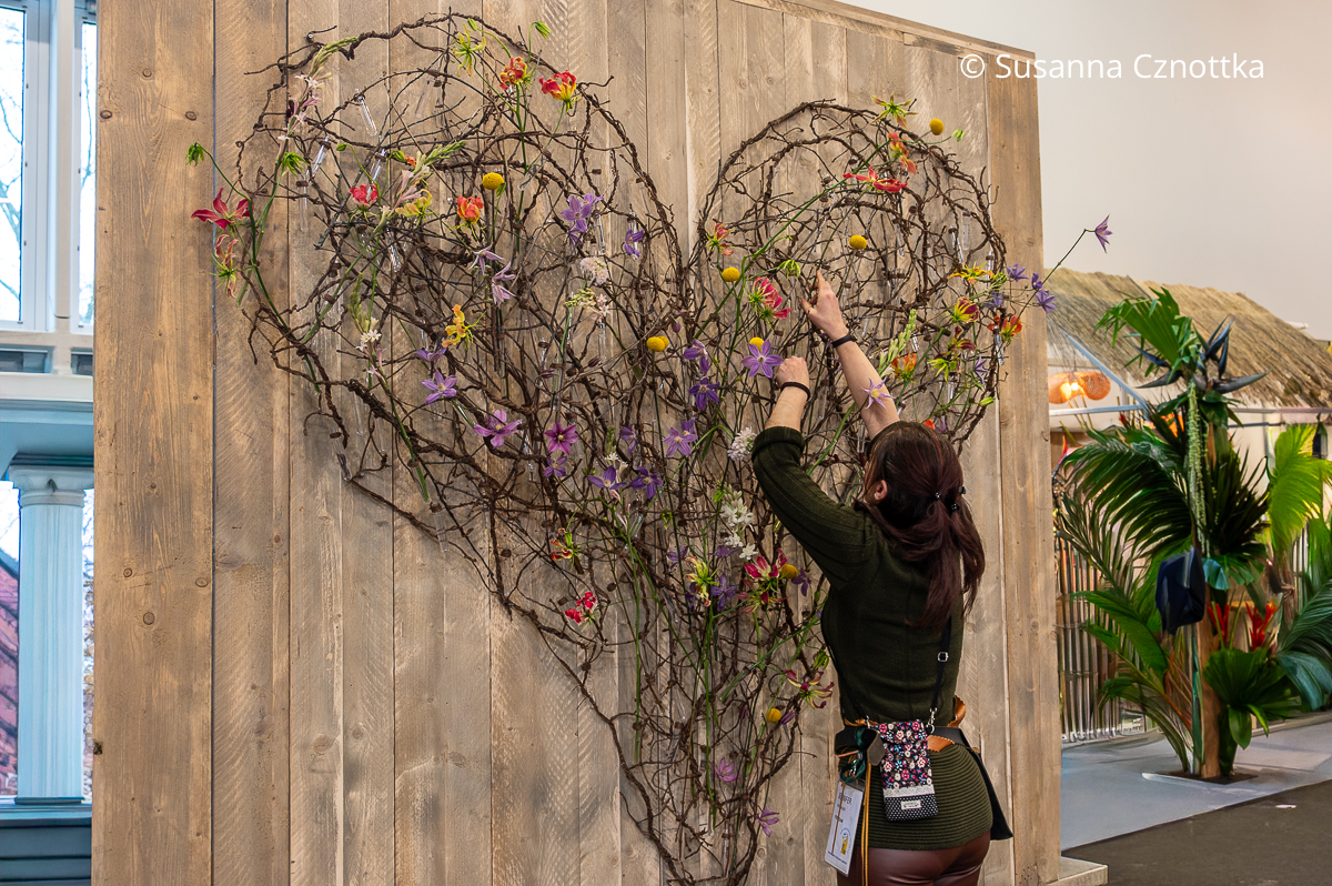 Eine Floristin steckt Blüten in ein florales Werkstück in Herzform