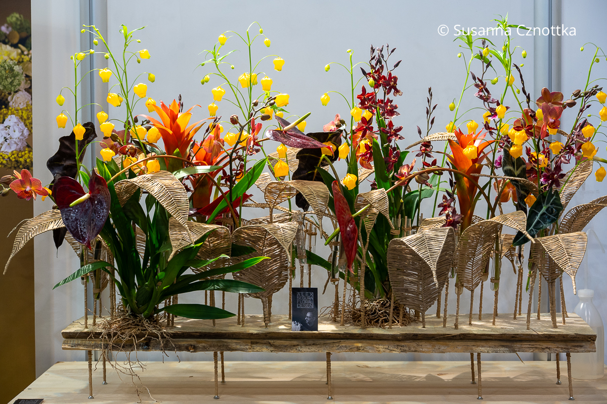 Gesteck aus exotischen Blüten in warmen Farben und künstlichen Blättern in Naturfarben