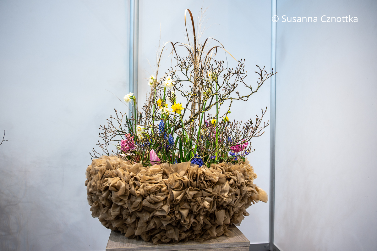 Pflanzschale aus naturfarbenem Gewebe mit Frühblühern, Ästen und Gräsern