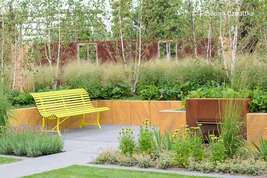 Ein Hochbeet aus gelben Betonelementen hebt die Bepflanzung aus kleinen Birken und Gräsern auf die Augenhöhe einer gelben Bank davor
