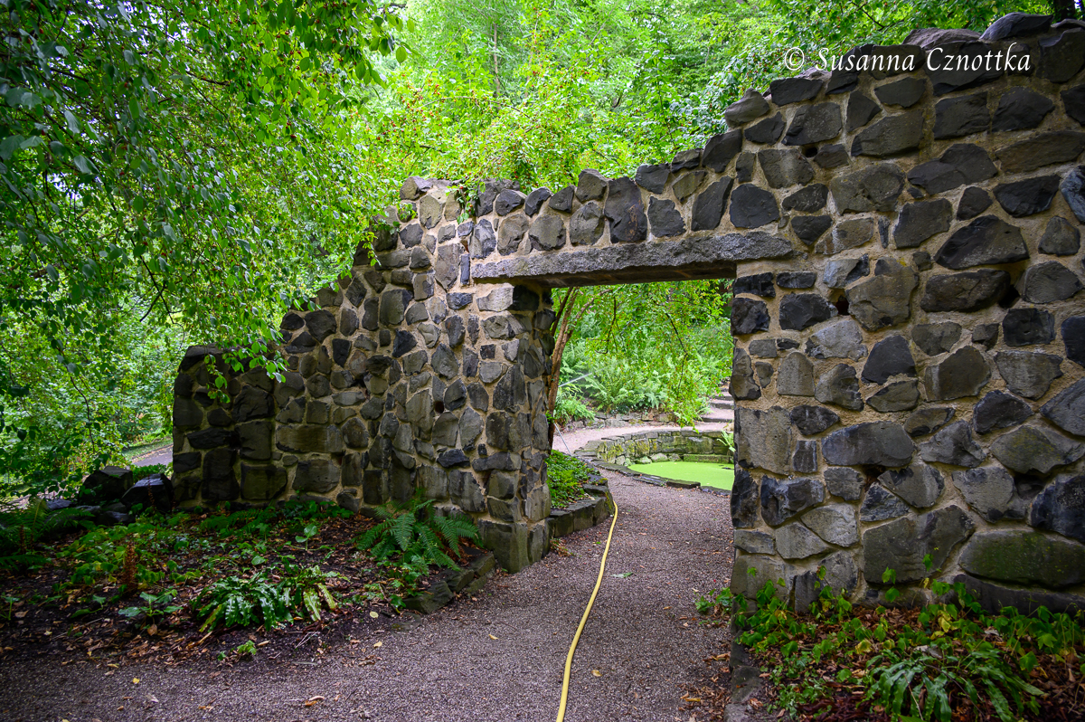 Eine freistehende Natursteinmauer als Eingang zu einem Gartenraum 