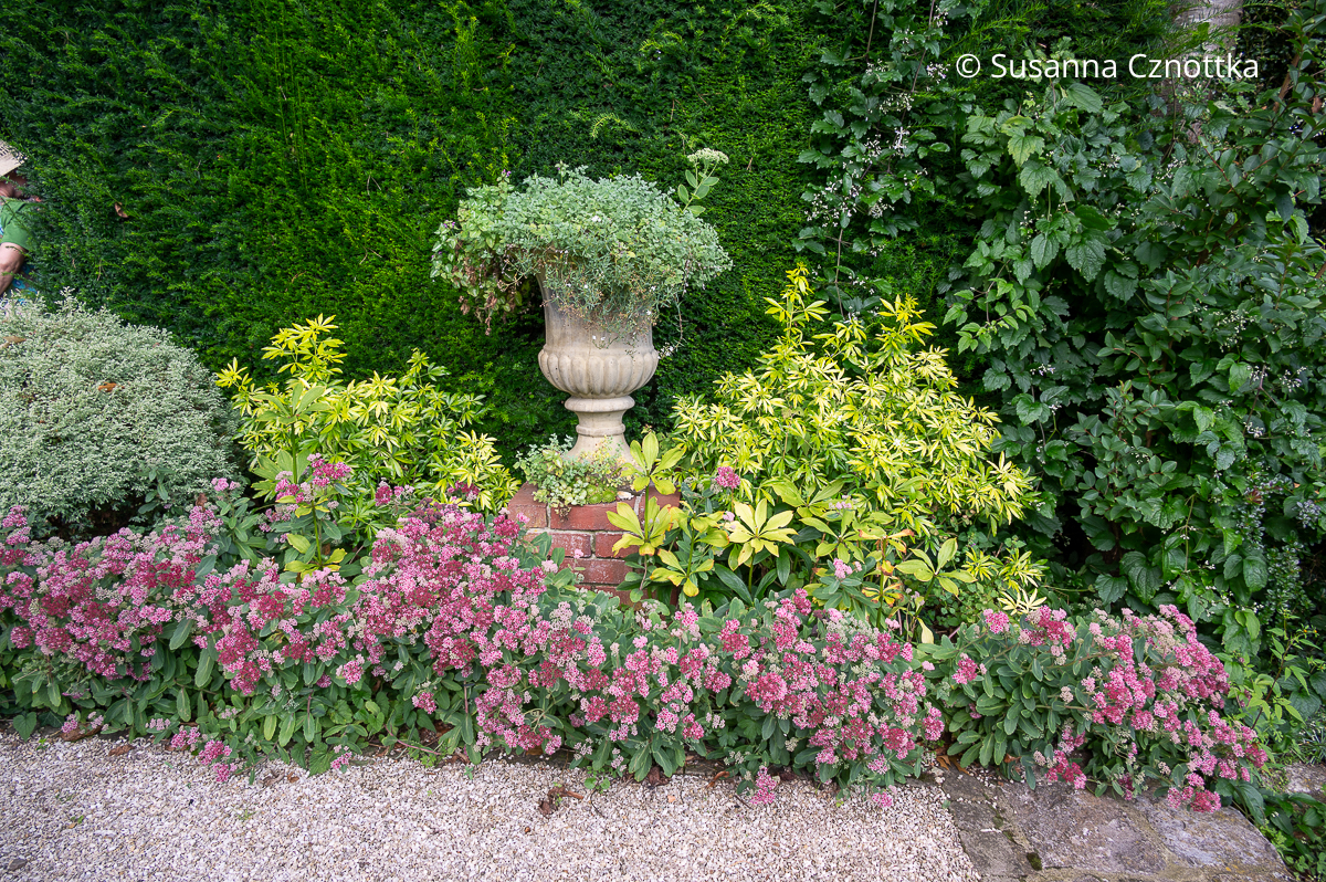 Blickpunkt im Garten: bepflanzte Vase auf einem gemauerten Podest