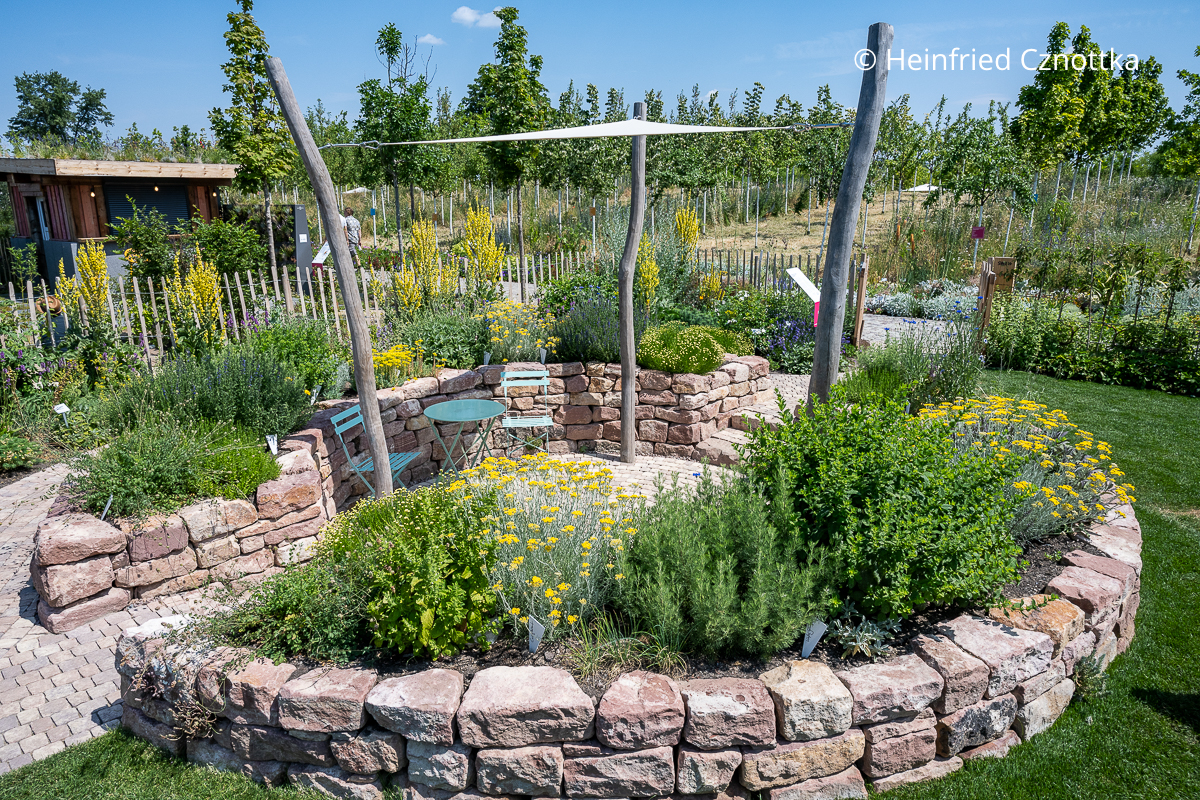 Ein Senkgarten mit Hochbeeten aus Naturstein, mit Kräutern bepflanzt