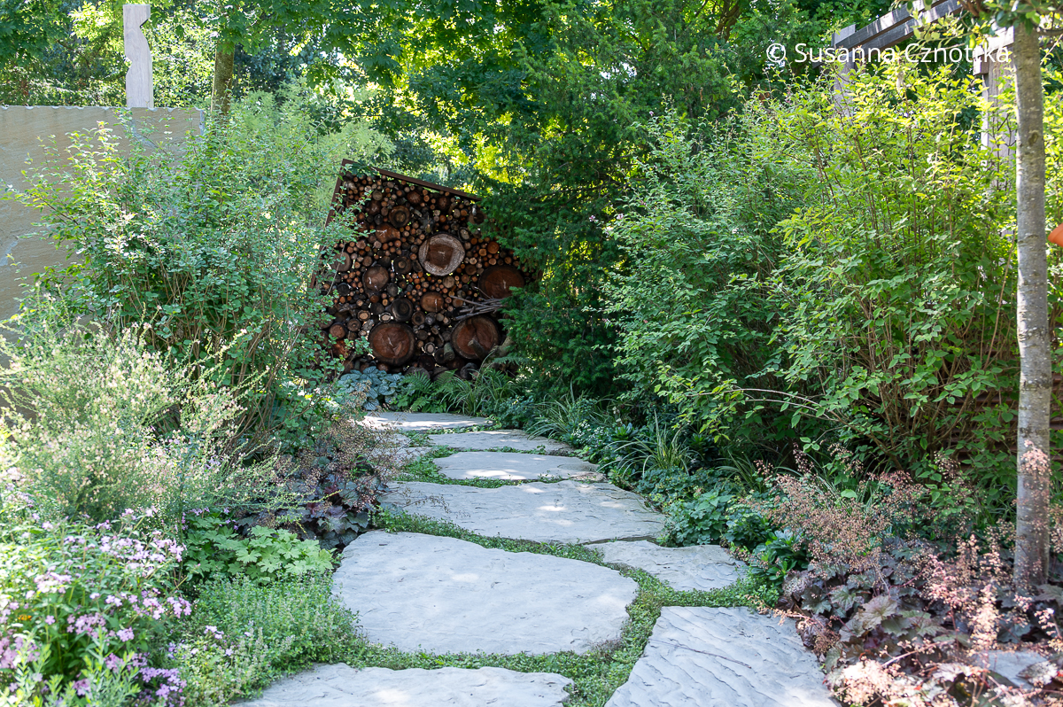 Ein Gartenweg aus großen Natursteinplatten Ein Gartenweg aus großen Natursteinplatten führt auf ein Holzlager aus Cortenstahl zu.