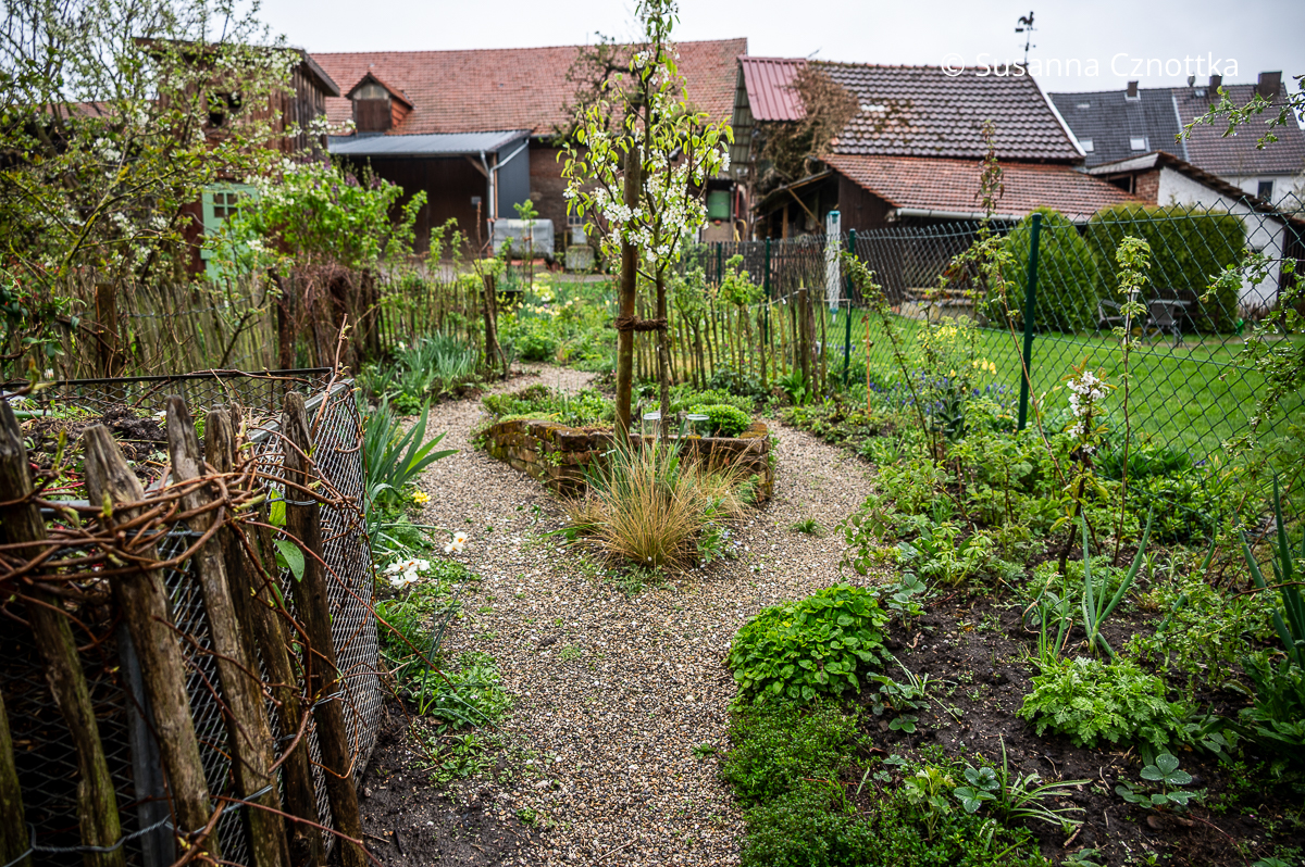 Gartenraum mit Kompost, Staketenzaun und kleinem Inselbeet
