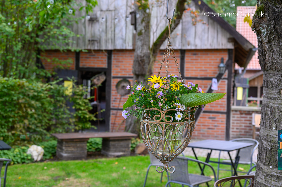 Eine Blumenampel hängt vor einem alten Backhaus
