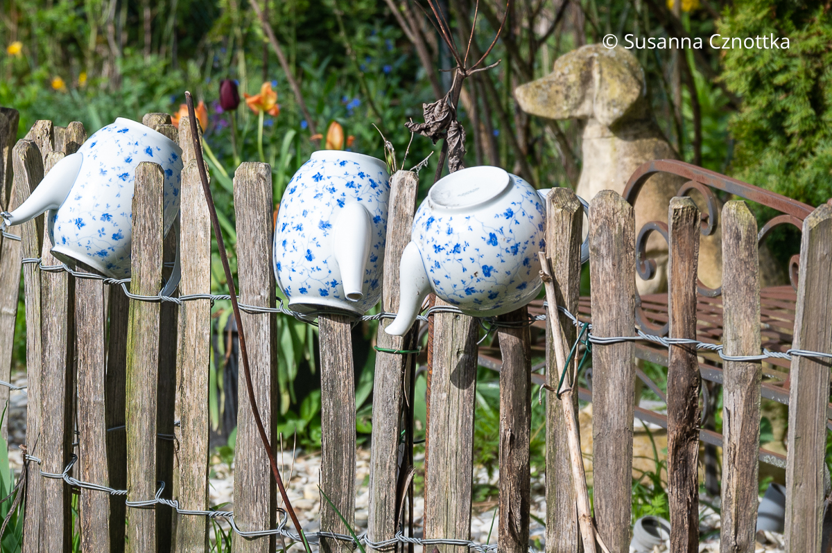Fröhliche Gartendeko: Teekannen auf einem Staketenzaun