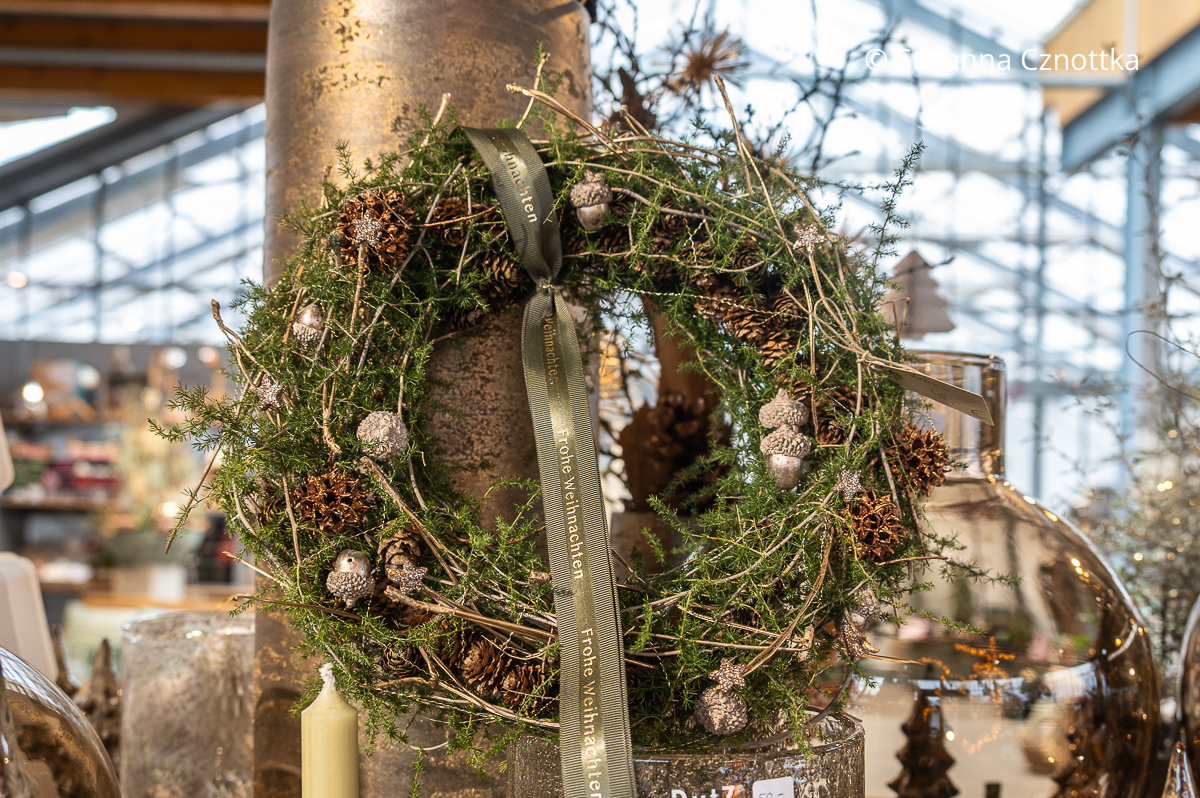 Weihnachtlicher Kranz ohne Kerzen aus Asparagus mit silbernen Eicheln und goldenen Früchten des Amberbaums mit einem grünen Schleifenband