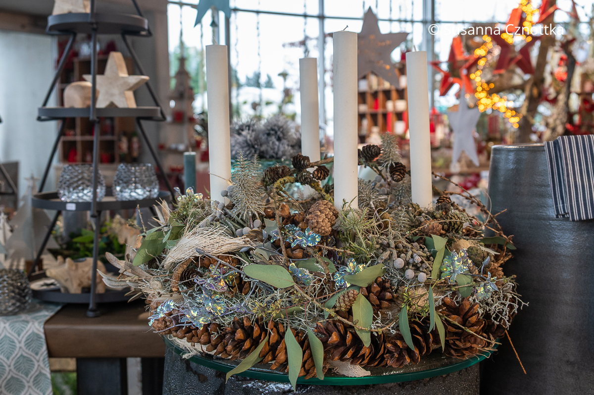 Weihnachtliche Deko: Adventskranz mit Zapfen, weißen Kerzen und einigen glänzenden Blättern in Türkis
