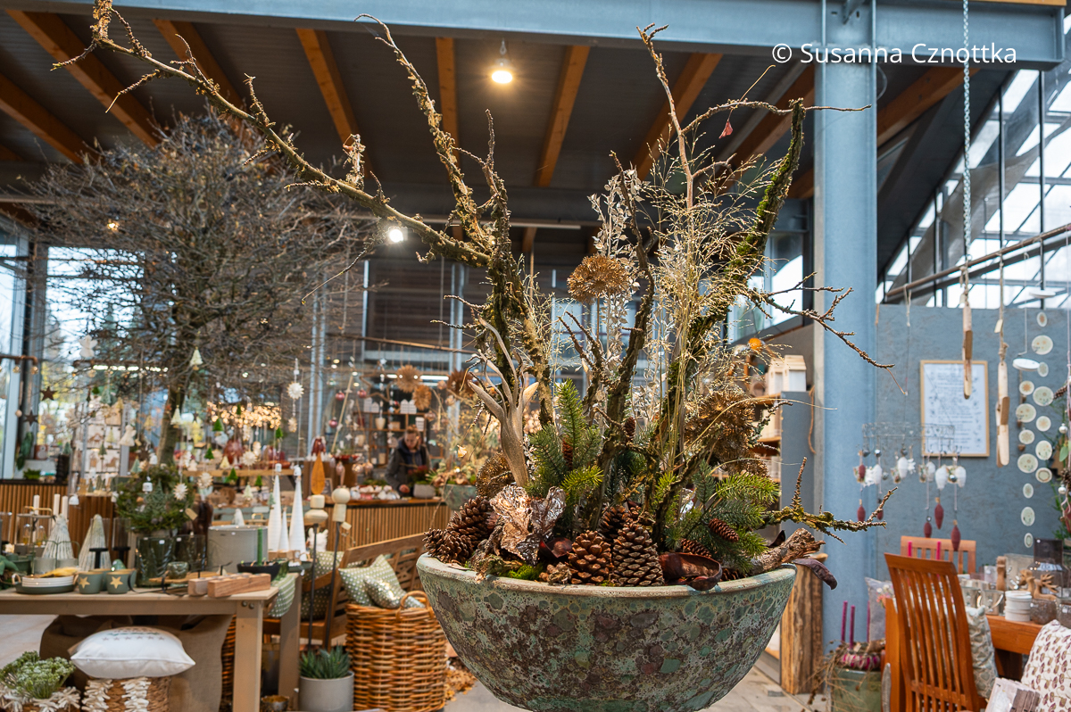 Ein opulentes Gesteck mit Zweigen, Gräsern, Zapfen und weiteren Details in einer großen Keramikschale mit türkis-braunem Muster