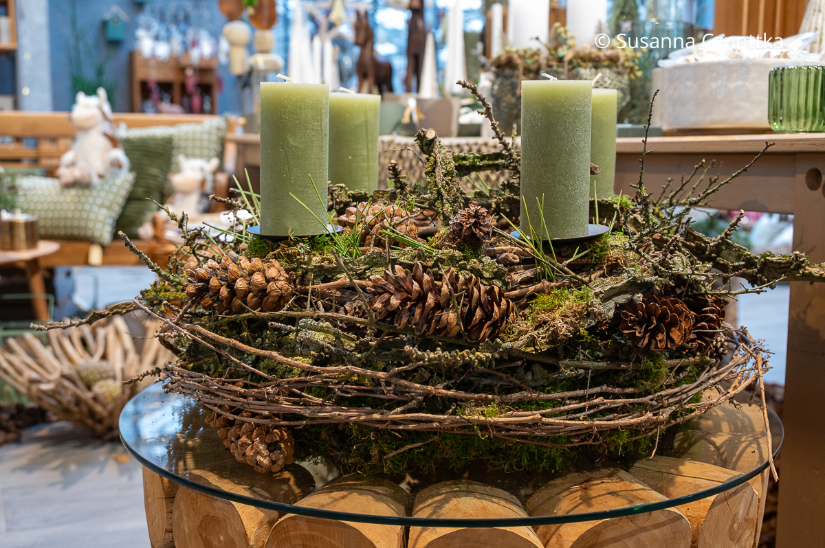 Ein Adventskranz mit grünen Kerzen aus Moos, mit Zweigen umwunden und mit Zapfen geschmückt