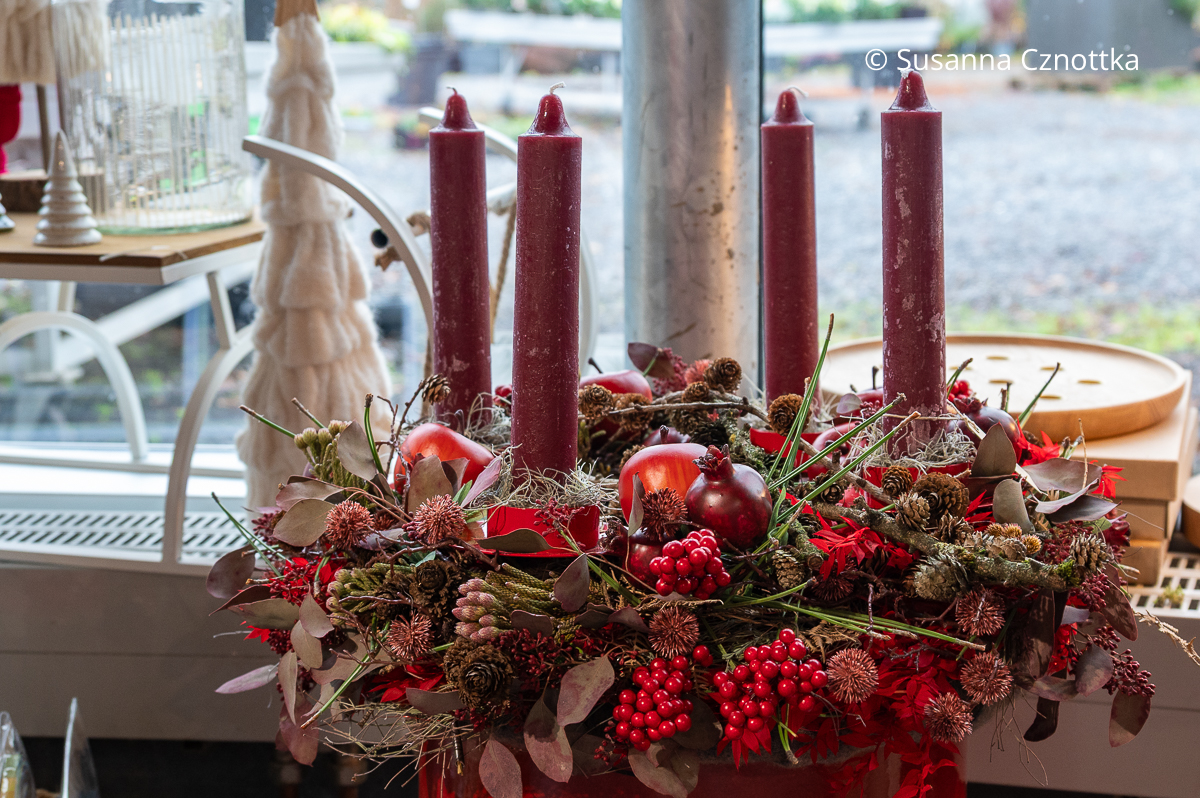 Üppiger Adventskranz in Rottönen mit Äpfeln und Granatäpfeln, Zapfen und vier dunkelroten Stabkerzen