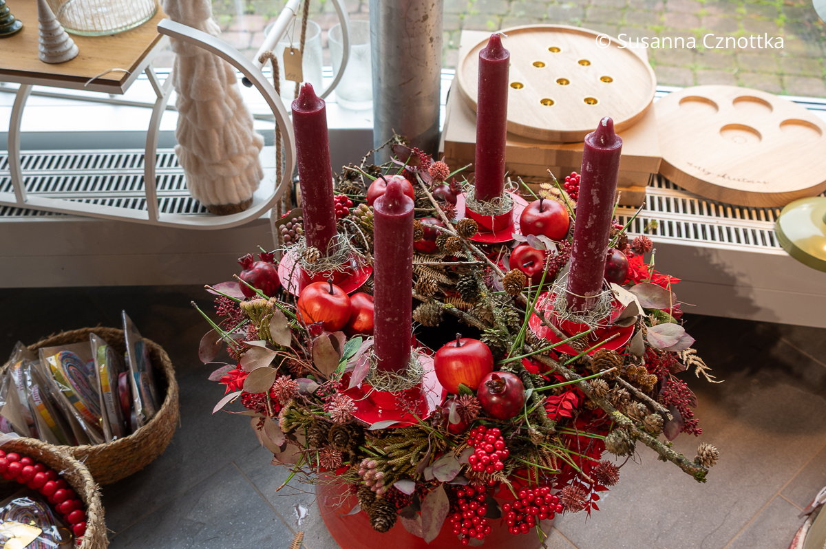 Üppiger Adventskranz in Rottönen mit Äpfeln und Granatäpfeln, Zapfen und vier dunkelroten Stabkerzen