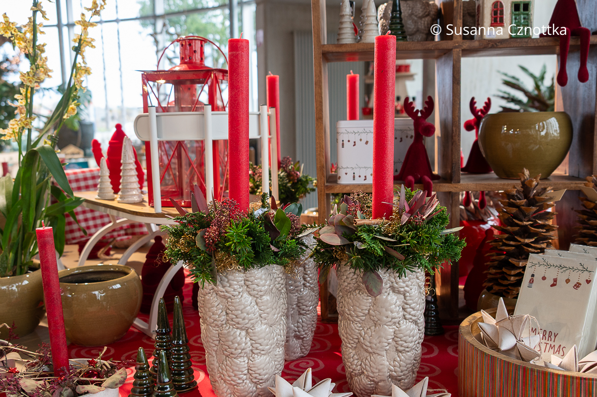 Schlanke Adventsgestecke in weißen Keramikgefäßen mit Zapfenstruktur und roten Stabkerzen