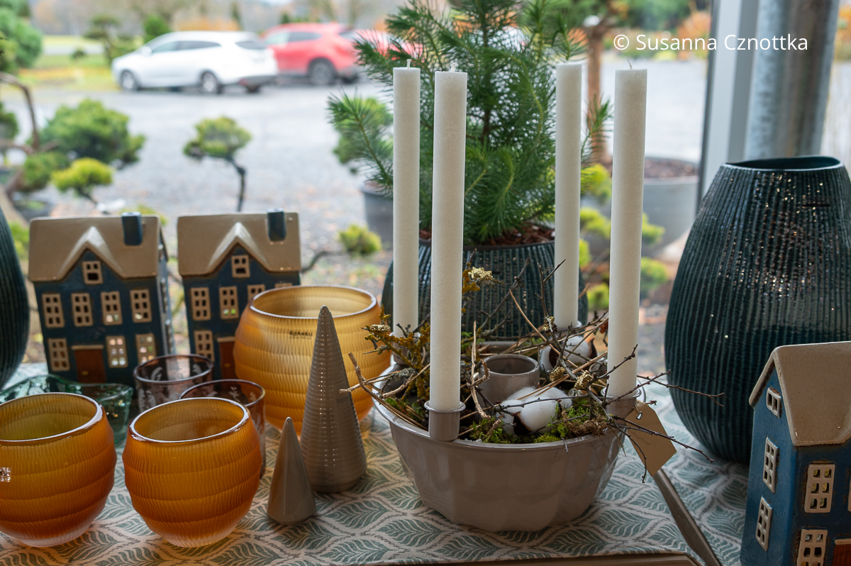 Eine beige Gugelhupfform mit Zweigen, Baumwolle und vier weißen Stabkerzen in Halterungen auf dem Rand