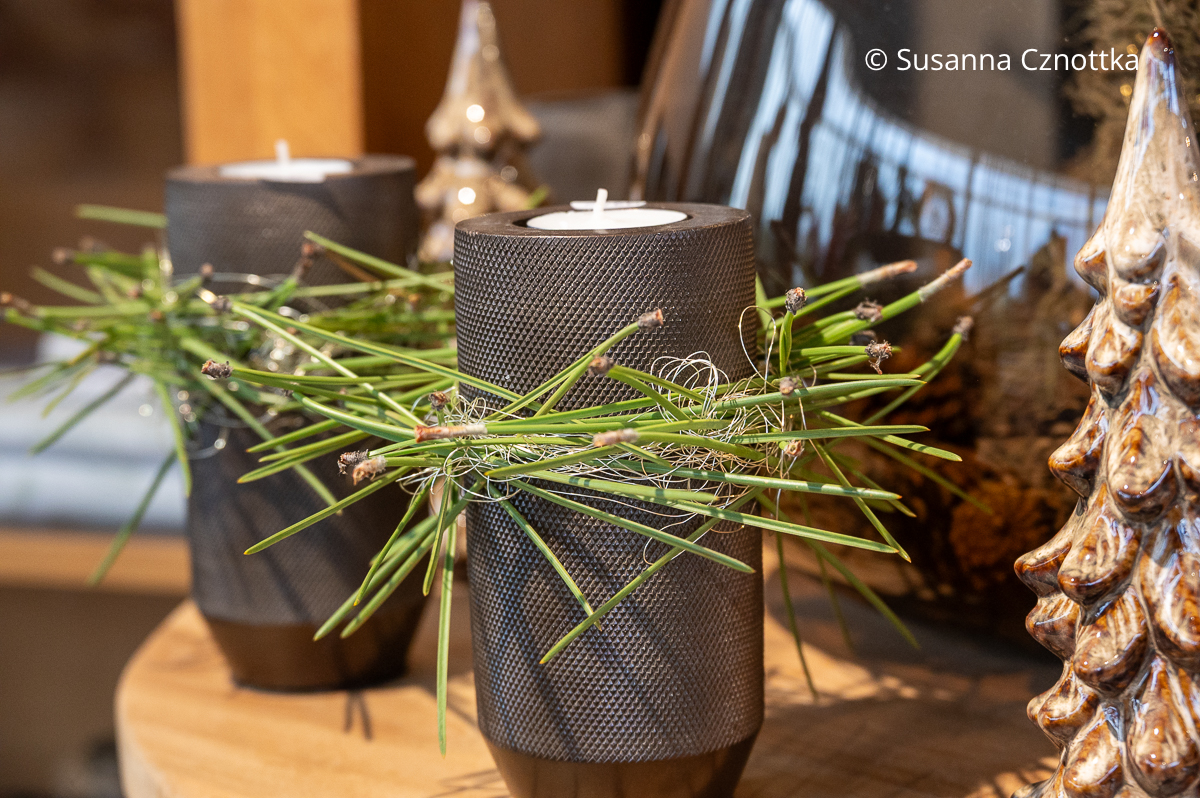 Schlichte graue Kerzenleuchter mit einem Kränzchen aus Piniennadeln und feinem silbernem Draht