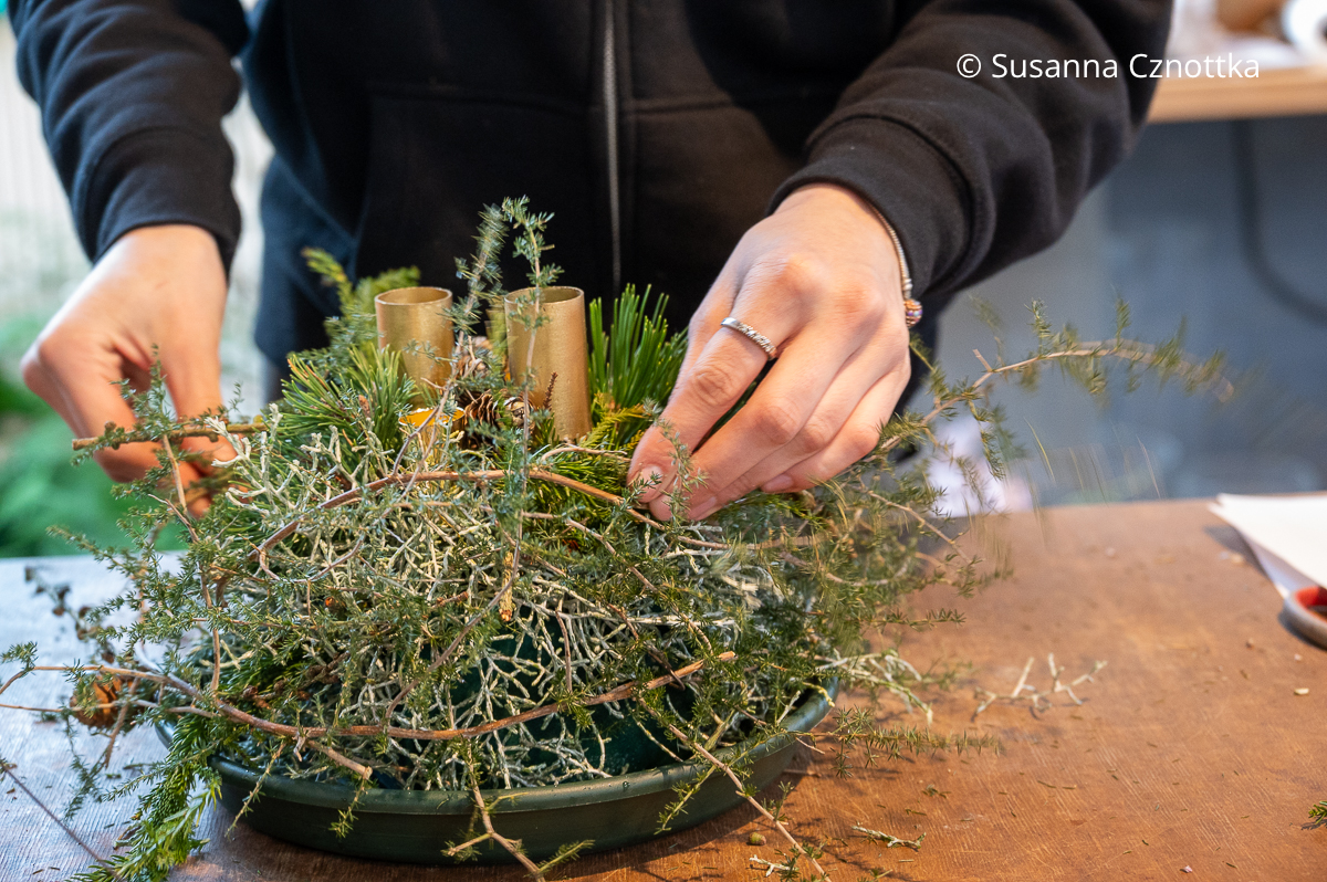 Eine Frau fügt einen Asparaguszweig in ein Gesteck ein