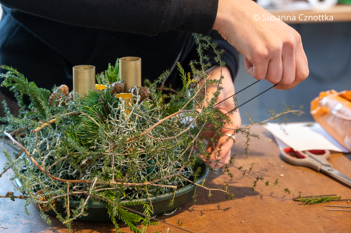 Eine Frau befestigt einen Asparaguszweig mit einem Draht an einem Gesteck