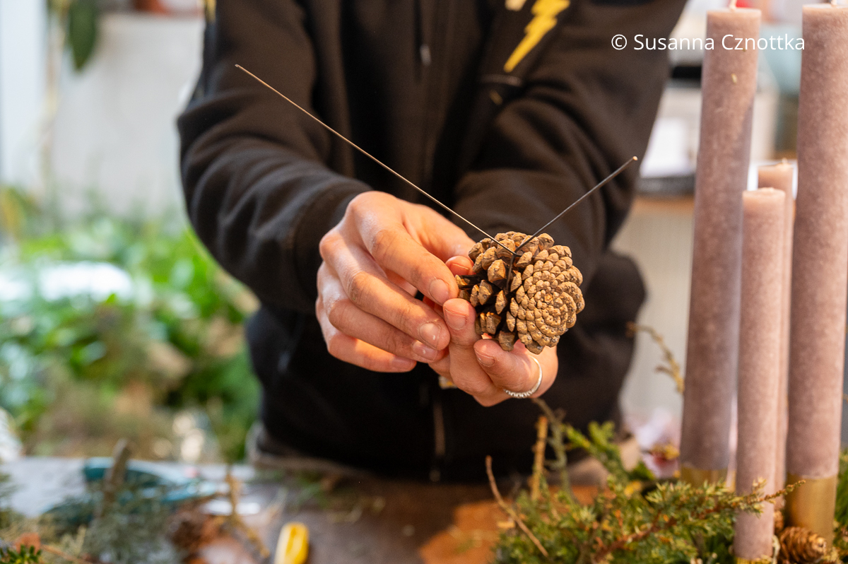 Eine Frau befestigt Draht an einem Kiefernzapfen