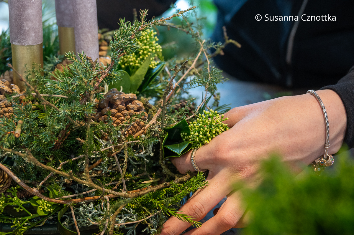 Eine Frau steckt grüne Knospen einer Blütenskimmie in ein Gesteck