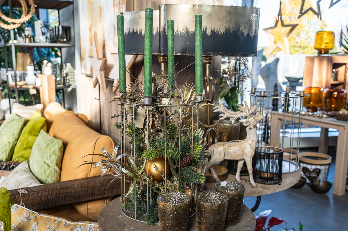 Ein mit Grün und Kugeln gefüllter runder Metallkorb mit vier grünen Stabkerzen in einer Halterung darauf