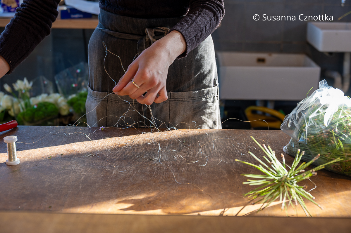 Eine Frau wickelt silbernen Draht von einer Rolle ab