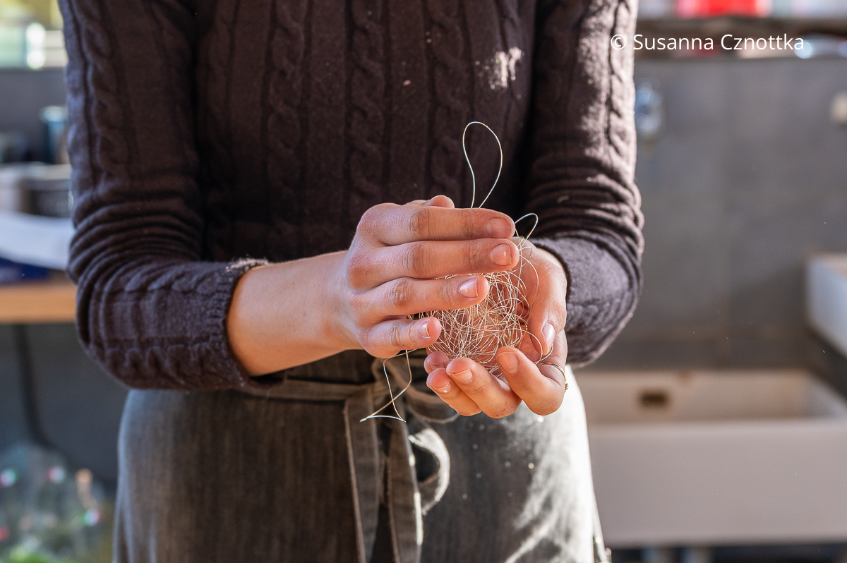 Eine Frau formt eine Kugel aus dünnem silbernem Draht