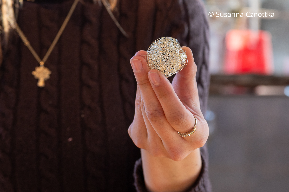 Die Hand einer Frau hält eine kleine Kugel aus feinem silbernem Draht