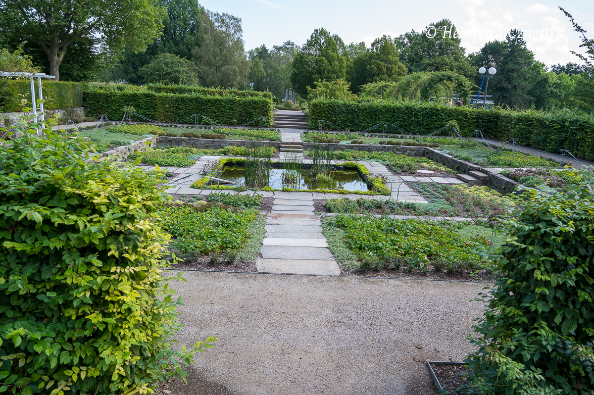 Ein streng geometrischer Senkgarten mit einem quadratischen Wasserbecken und geraden Wegen aus Steinplatten