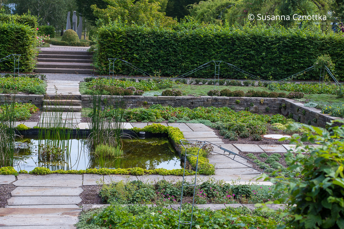 Ein Senkgarten mit einem quadratischen Wasserbecken und geraden Wegen