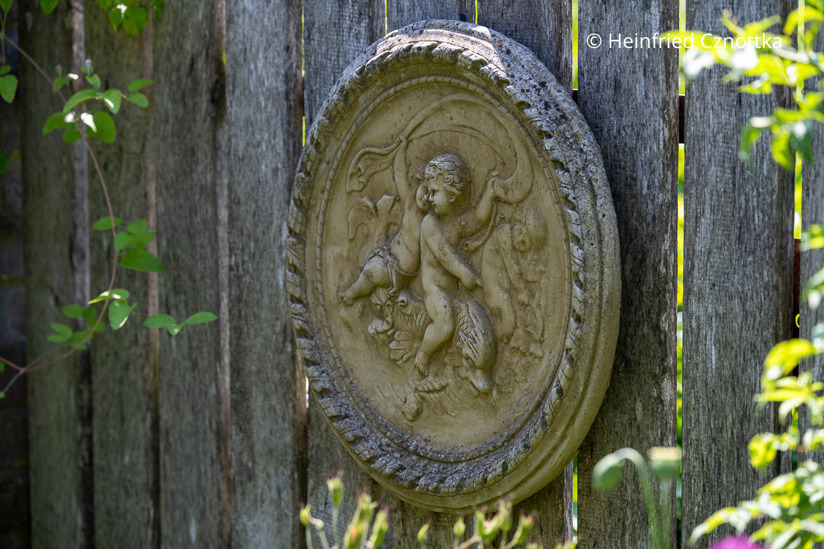 Ein Wandrelief mit klassischem Putten-Motiv als Gartendekoration Ein Wandrelief mit klassischem Putten-Motiv als Gartendekoration an einem Holzzaun